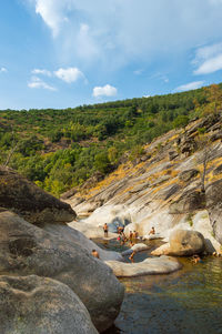 People on rocks by river against sky