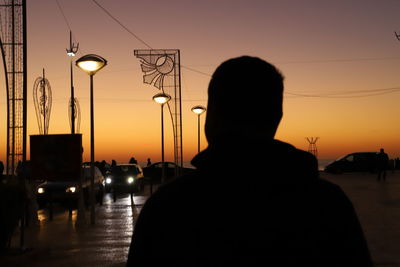 Silhouette man and illuminated street light against orange sky