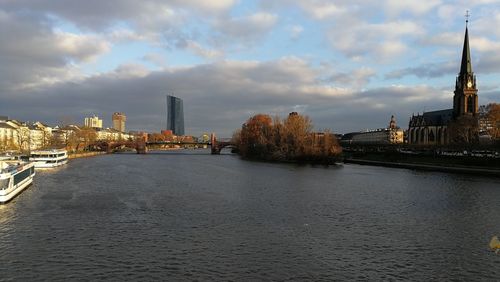 River amidst buildings in city against cloudy sky