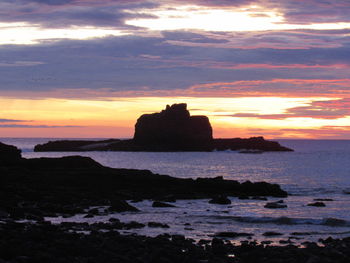 Silhouette rocks on shore against sky during sunset