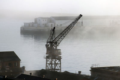 Crane by pier on sea against sky