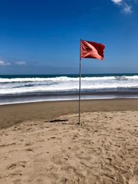 Red flag waving at beach against blue sky