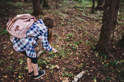 Girl with backpack holding stick while bending in forest