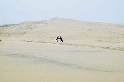 People on sand dune against clear sky