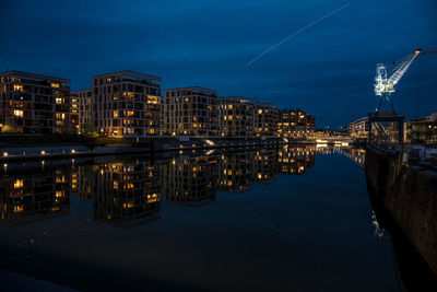 Illuminated buildings by river against sky at night