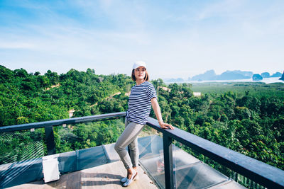 Portrait of young woman standing on railing against trees