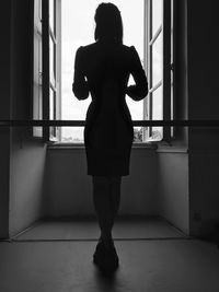 Rear view of woman standing against window at home