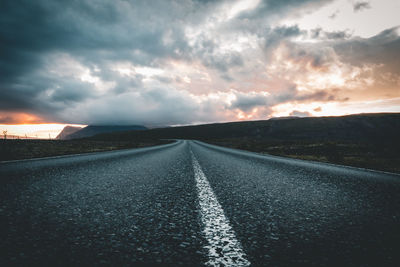 Surface level of empty road against cloudy sky during sunset