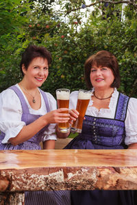 Portrait of smiling friends toasting drinks while sitting at table outdoors