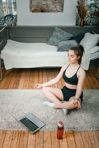 Cheerful sportswoman with blond hair meditates in lotus position, resting on the floor at home 