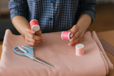 Top view of a dressmaker holding spools of thread near a piece of fabric and scissors