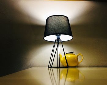 Close-up of illuminated lamp on table against wall