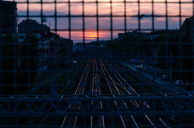 Railroad tracks seen through fence during sunset