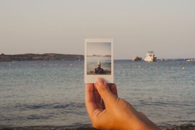 Midsection of person holding sea against clear sky