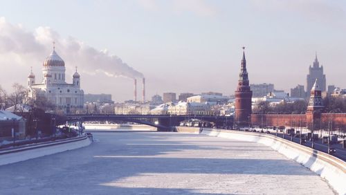 Frozen river amidst buildings against sky