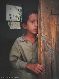 Portrait of boy looking away while standing against door