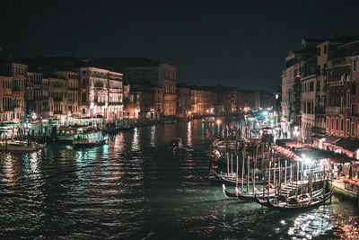 Sailboats moored on canal by illuminated buildings in city at night