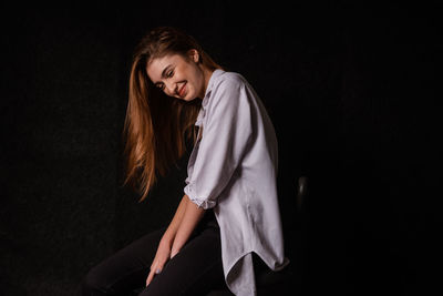 Beautiful young woman sitting against black background