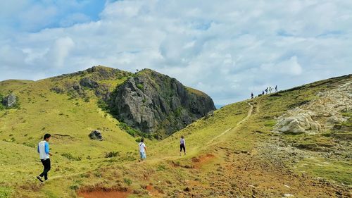 Hikers on hill against cloudy sky