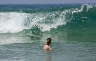 Friends swimming by wave in sea