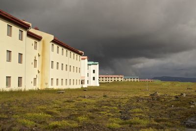 Buildings by grassy field against cloudy sky