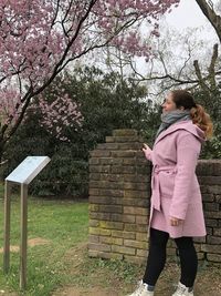 Rear view of woman standing by pink cherry blossom