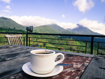 Coffee cup on table by mountains against sky