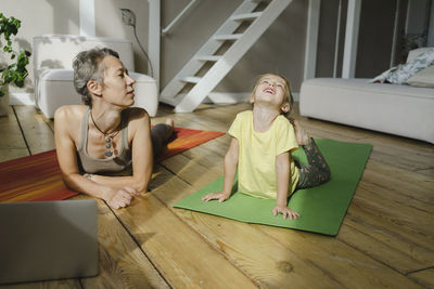Mother looking at daughter doing cobra pose on mat