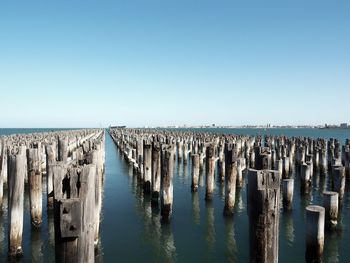 Wooden posts in sea against clear sky