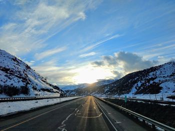 Road amidst snowcapped mountains against sky during winter
