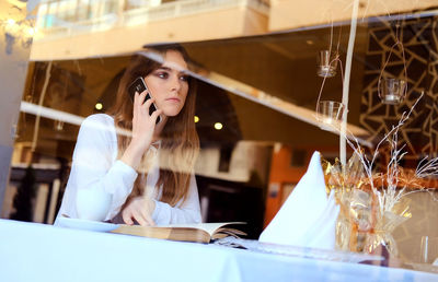 Close-up of teenager talking on mobile phone while sitting in restaurant
