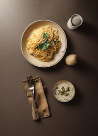 Top view of a plate with spaghetti next to a fork and on a brown table. image created by artificial intelligence and later modified