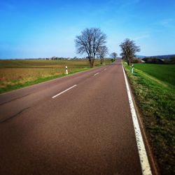 Empty road amidst field against sky