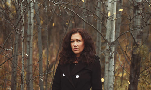 Portrait of young woman standing by bare trees in forest