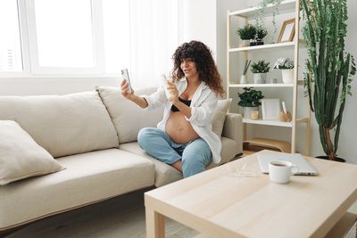 Side view of woman using digital tablet while sitting on sofa at home