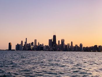 Sea and buildings against clear sky during sunset