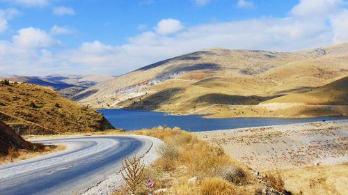 Empty road passing by river amidst mountains