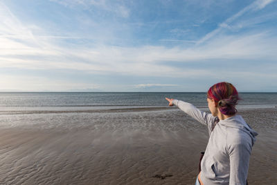 Woman pointing towards sea against sky