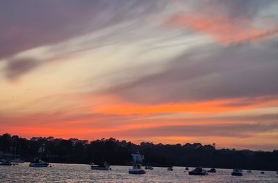 Sailboats moored on sea against dramatic sky during sunset