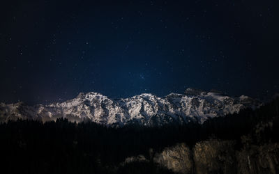 A beautiful night unfolds as a mountain range sparkles in winter, beneath a starlit sky.
