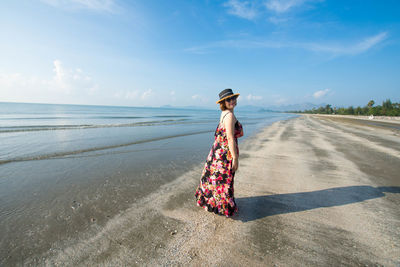 Side view of woman standing on sand at beach against sky