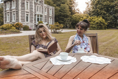 Couple of mature friendly women on vacation drinking tea and reading a book outdoors