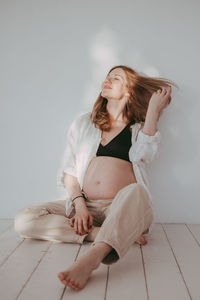 Beautiful caucasian pregnant woman in neutral clothes in white room, mom to be. motherhood 