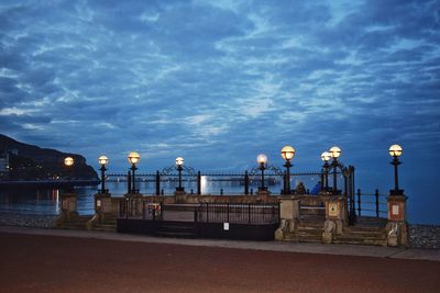 Illuminated street light by sea against sky