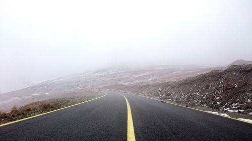 Country road leading towards mountains during foggy weather