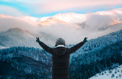 Man with arms outstretched against snowy mountain at sunset during winter