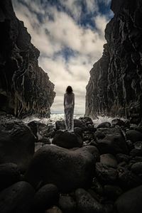 Rear view of people sitting on rock by sea against sky
