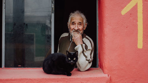 Portrait of senior man standing with cat on window