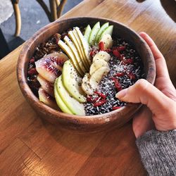 High angle view of hand holding fruits in bowl on table