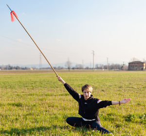 Caucasian young woman practicing wushu martial art on a green meadow with a long spear